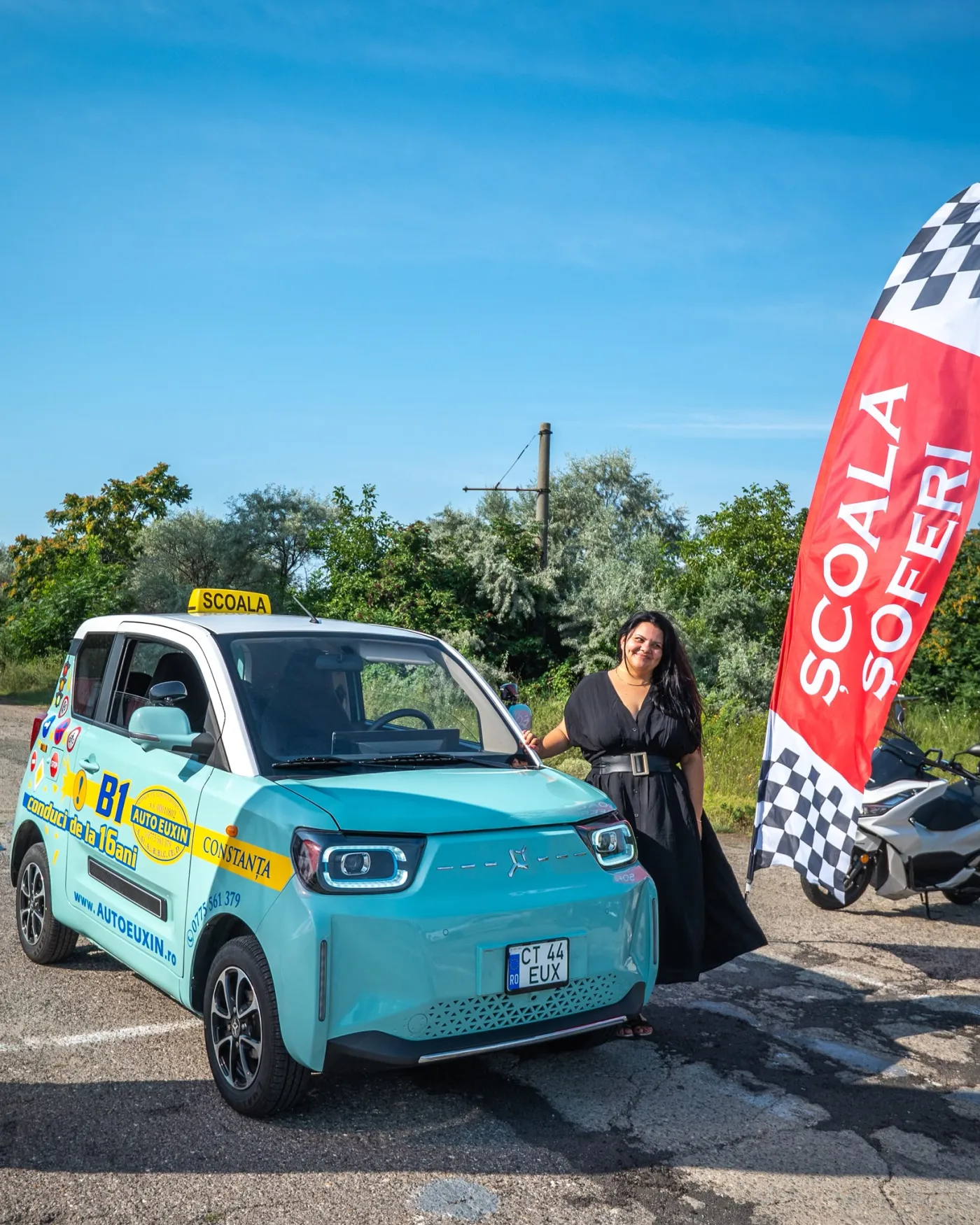 Mașina electrică B1 inscripționată „conduci de la 16 ani”, cu o cursantă alături