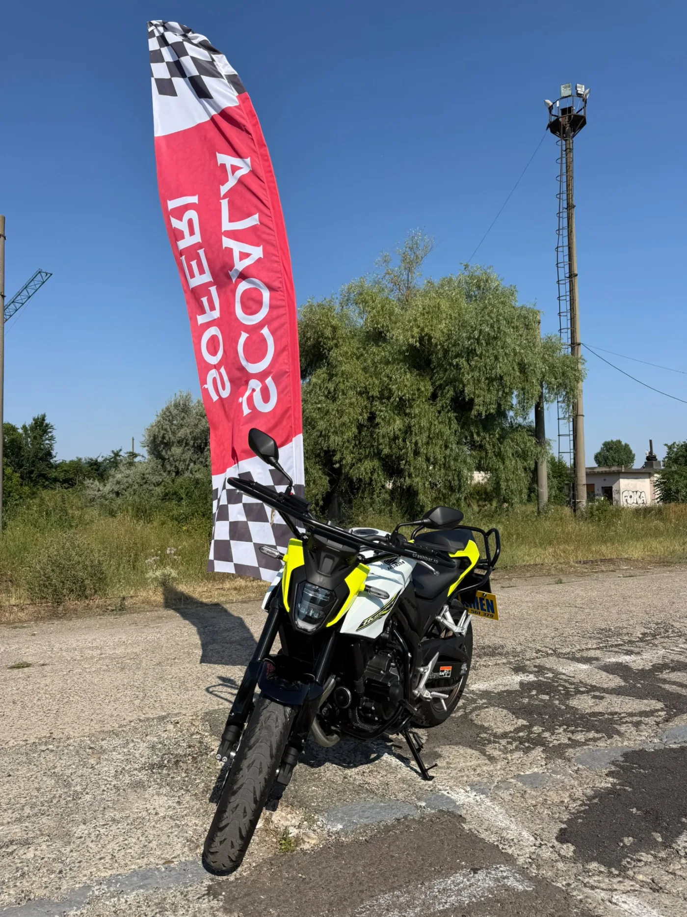 Honda CB125R galben cu negru, lângă bannerul Școala de Șoferi